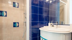 Une salle de bain avec un lavabo blanc, des carreaux bleus et un espace douche.