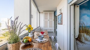 Een balkon met een houten tafel, planten in potten en uitzicht op het strand.