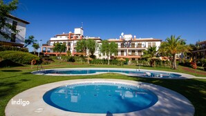 A hotel with a large swimming pool, palm trees, and a clear blue sky.