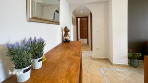 A hallway with a wooden table, two potted plants, a mirror, and a door leading to another room.