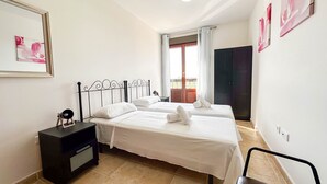 A hotel room with two beds, a dark nightstand, a small table, and a chair.