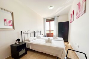 A hotel room with two beds, a dark nightstand, a small table, and a chair. - JAN001 Modern Spacious 2 Bedroom Apartment (Ayamonte)