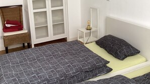 Une chambre avec deux lits, une armoire, une chaise et une table de chevet avec une lampe.