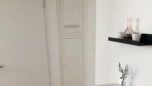 Une pièce avec une porte blanche, une armoire blanche, un plancher en bois et une étagère noire ornée d’objets décoratifs.