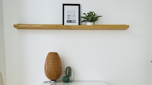 Ett rum med en trästol, en vit byrå, en flätad korg, en kaktus och ett inramat certifikat på en trähylla.