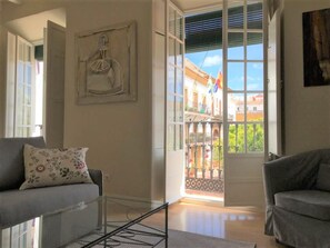 A spacious living room with a large window, a sofa, and a chair. - Suite - Orange Square Marbella (Marbella)