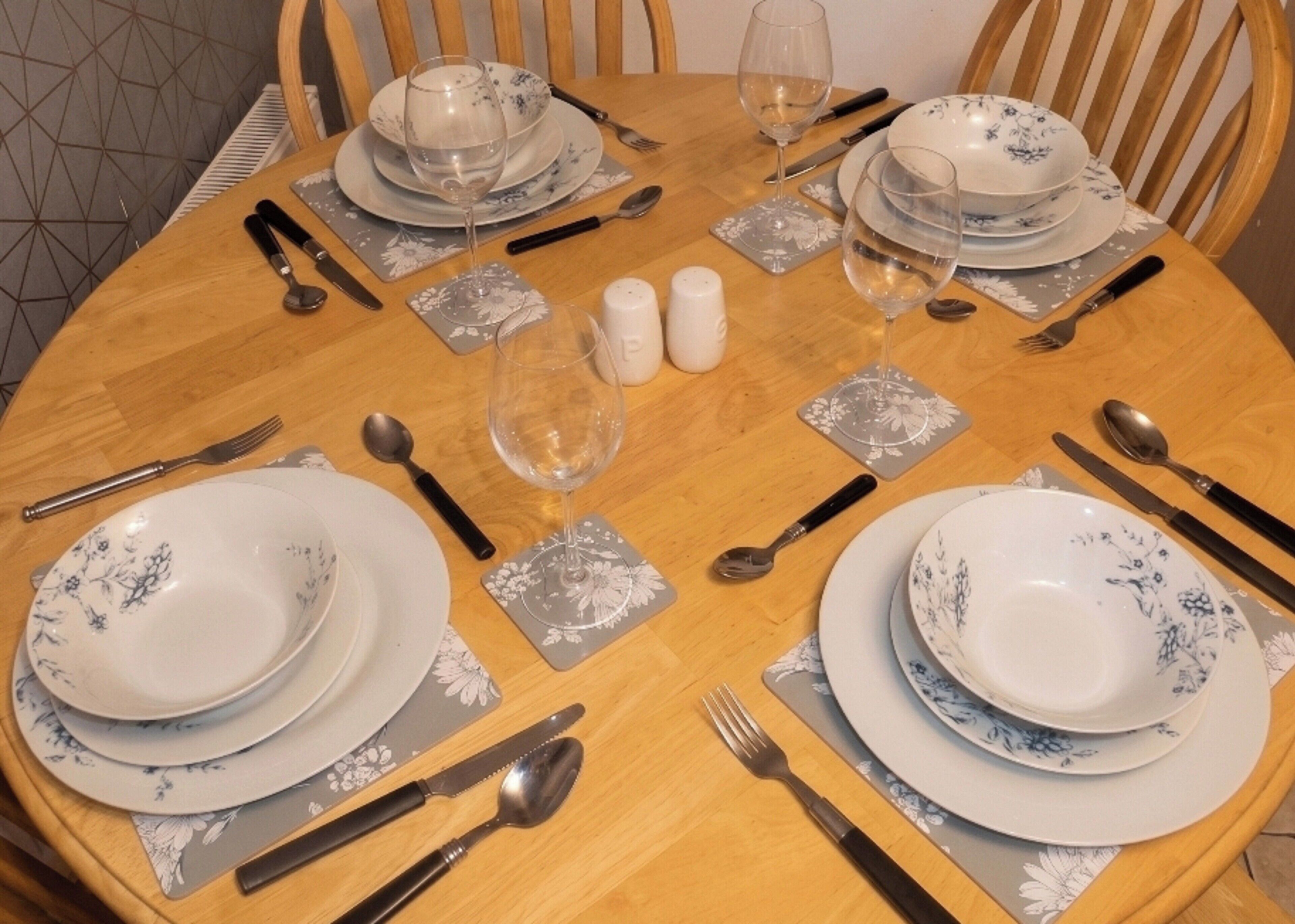 Uma mesa de jantar redonda posta com pratos, copos, talheres e saleiro e pimenteiro.