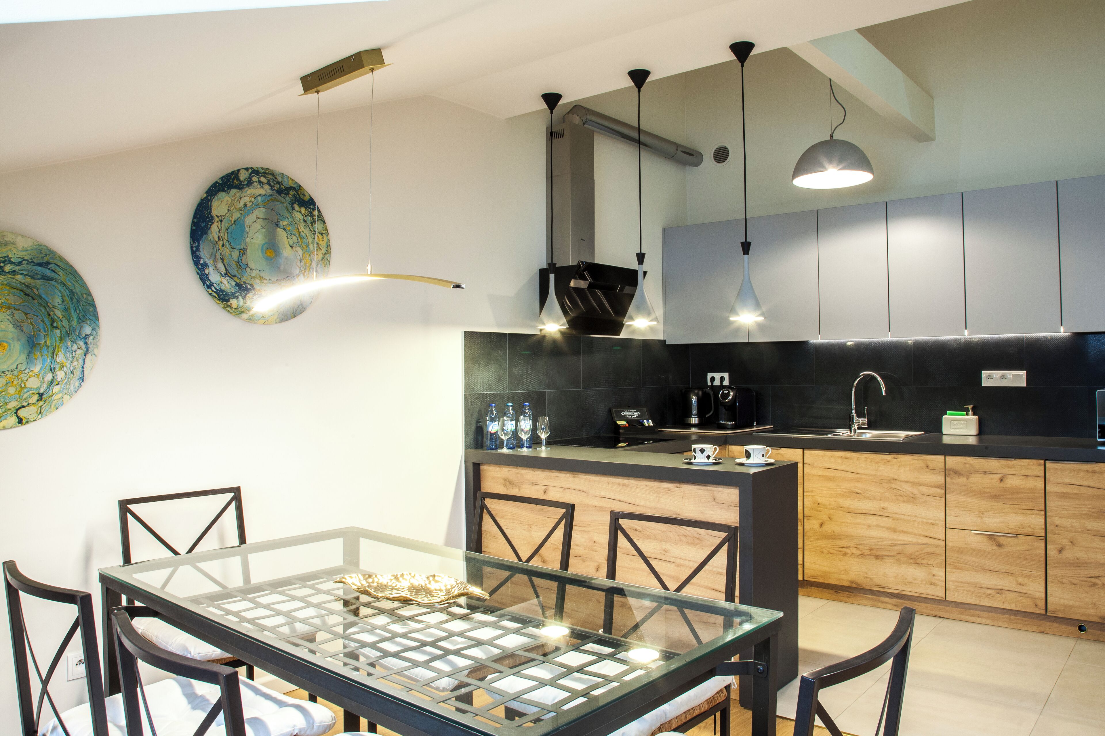 A modern kitchen with a glass dining table, wooden cabinets, and pendant lighting.