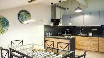 A modern kitchen with a glass dining table, wooden cabinets, and pendant lighting.