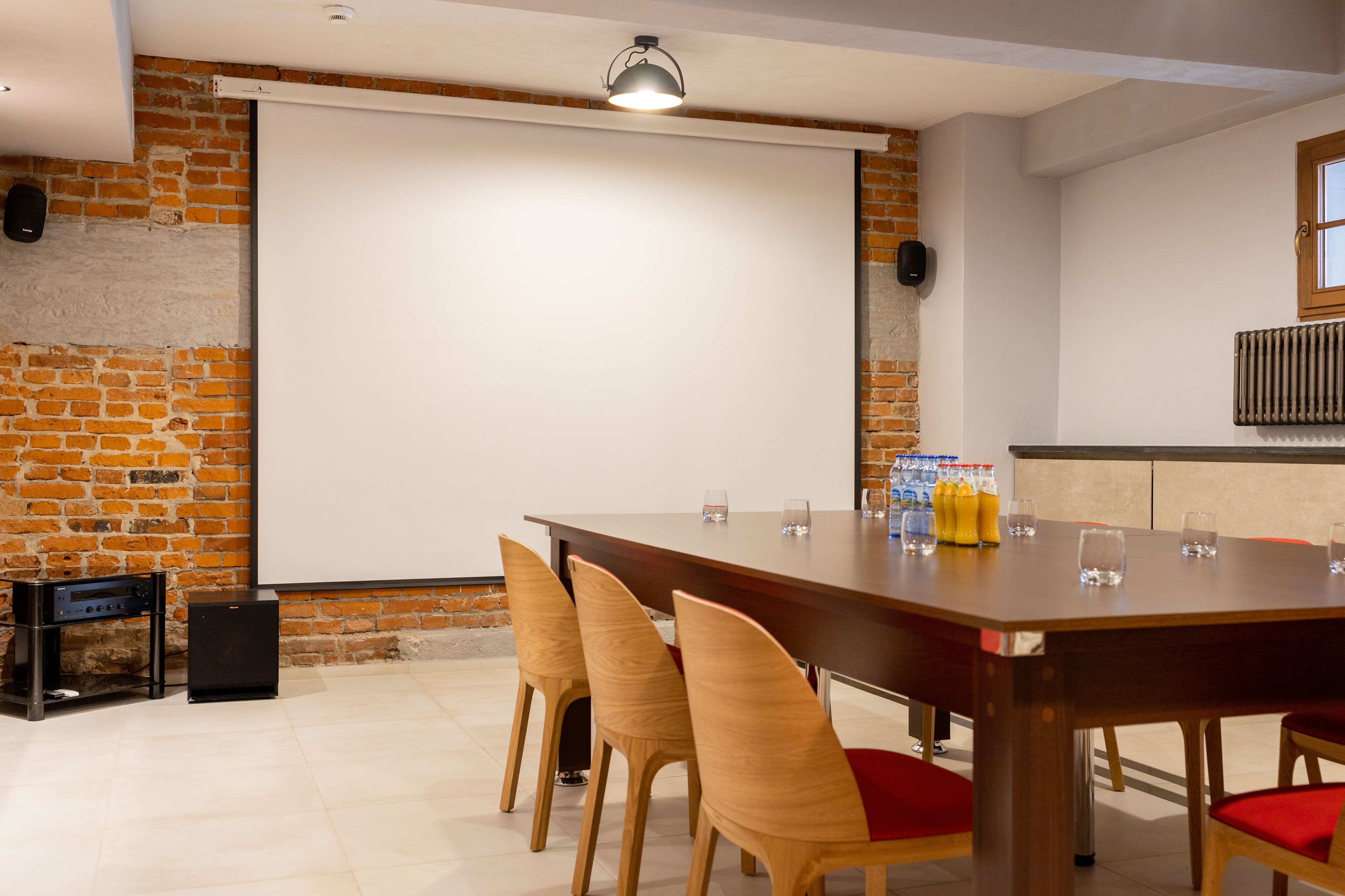 Un salón de conferencias con una mesa grande, sillas, una pantalla de proyector y un orador.