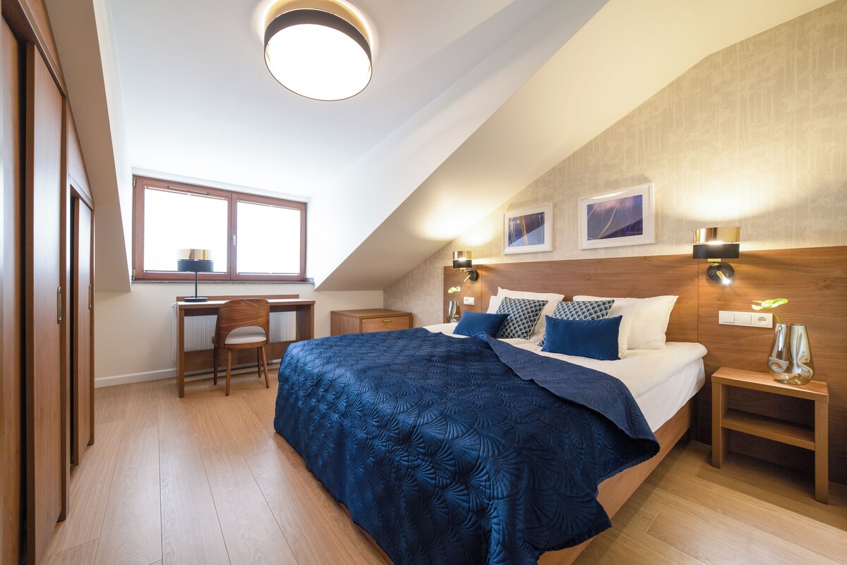 Un dormitorio con una cama grande, un escritorio, una silla y dos lámparas fijadas a la pared.