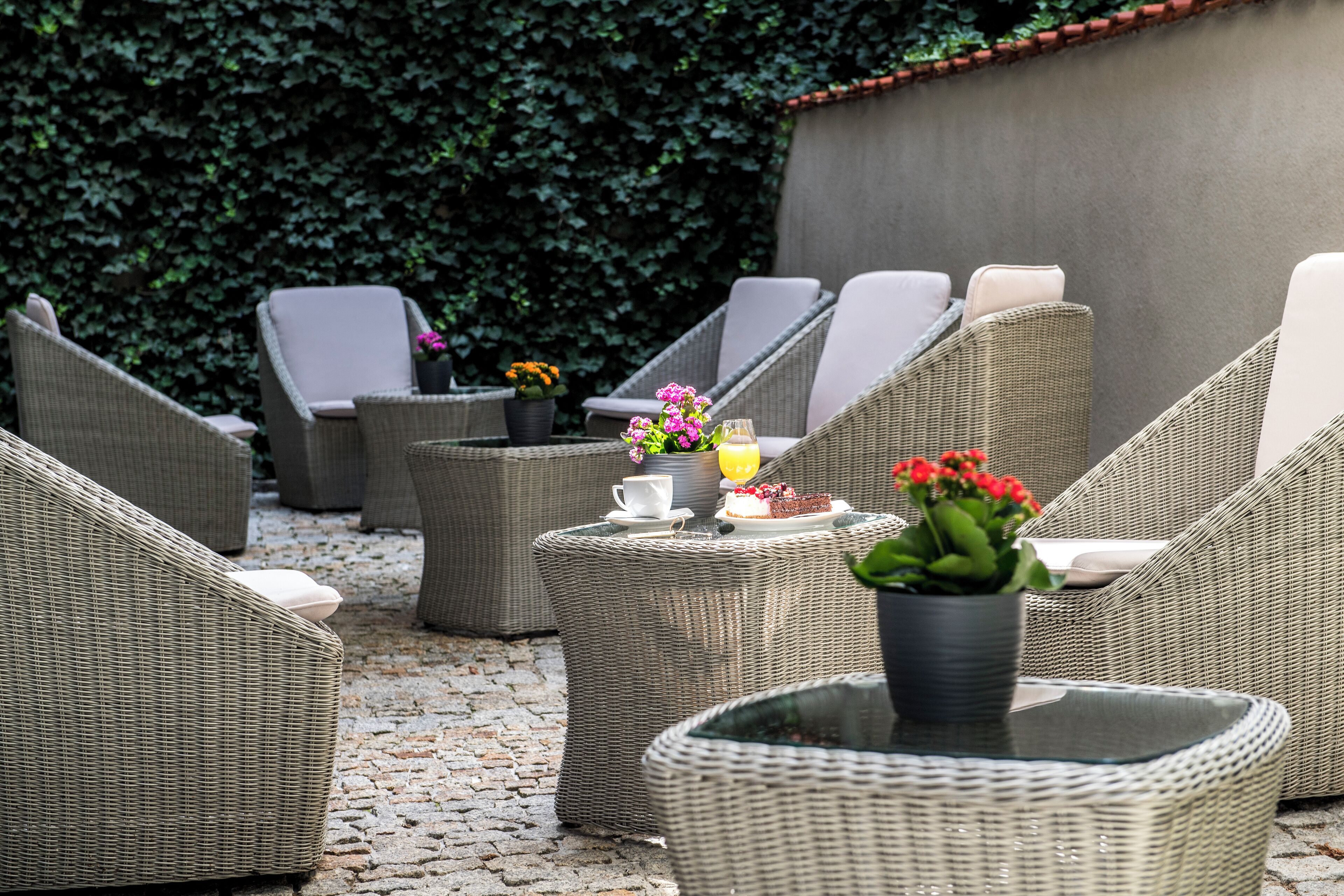 A patio area with wicker furniture, including chairs and a table, with a potted plant and a small table with a cup and a plate of food.