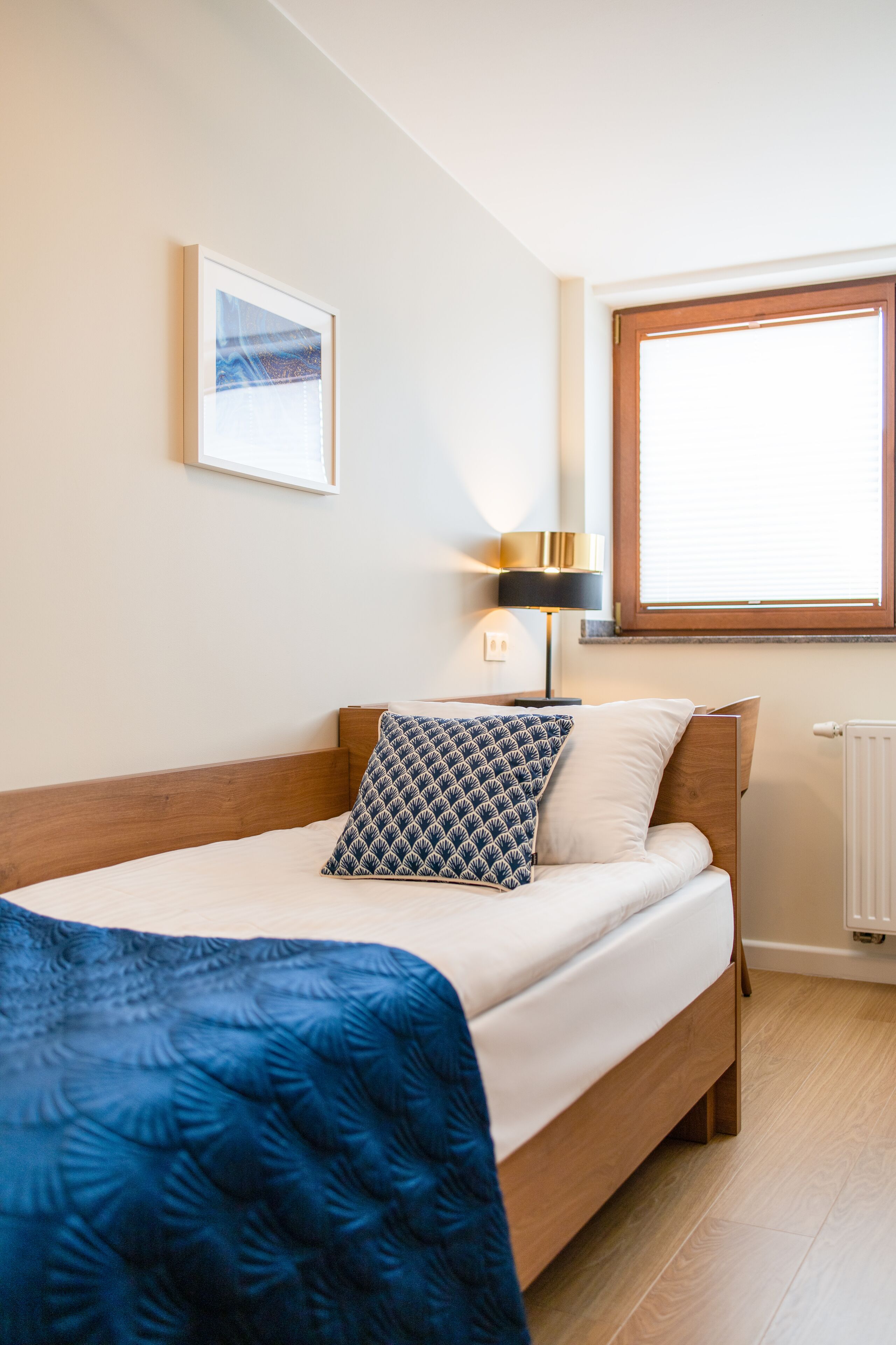 A neatly made bed with a blue blanket, a wooden headboard, and a bedside lamp.