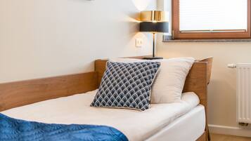 A neatly made bed with a blue blanket, a wooden headboard, and a bedside lamp.