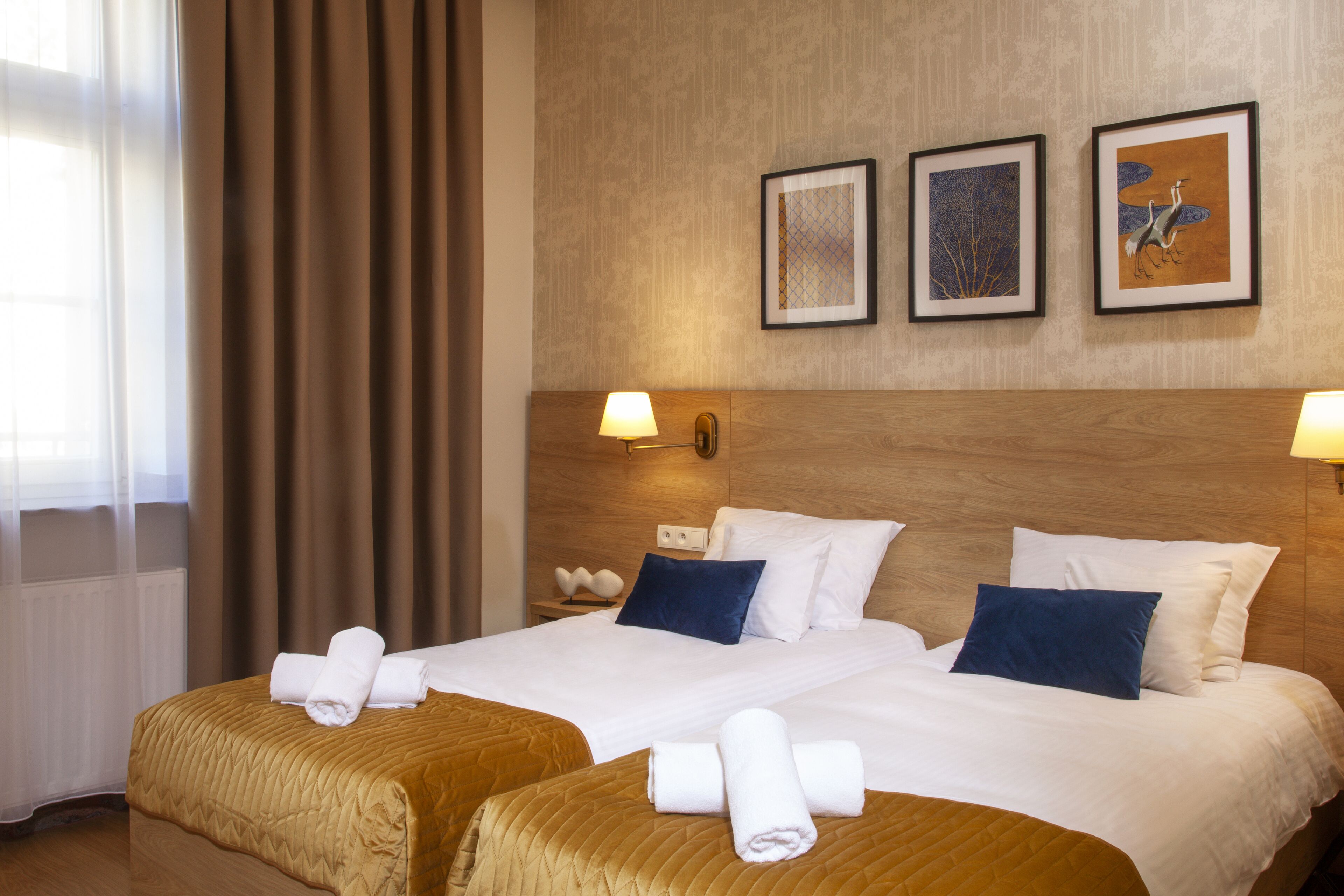 Een hotelkamer met twee bedden, een houten hoofdbord en drie kunstwerken in een lijst aan de muur.