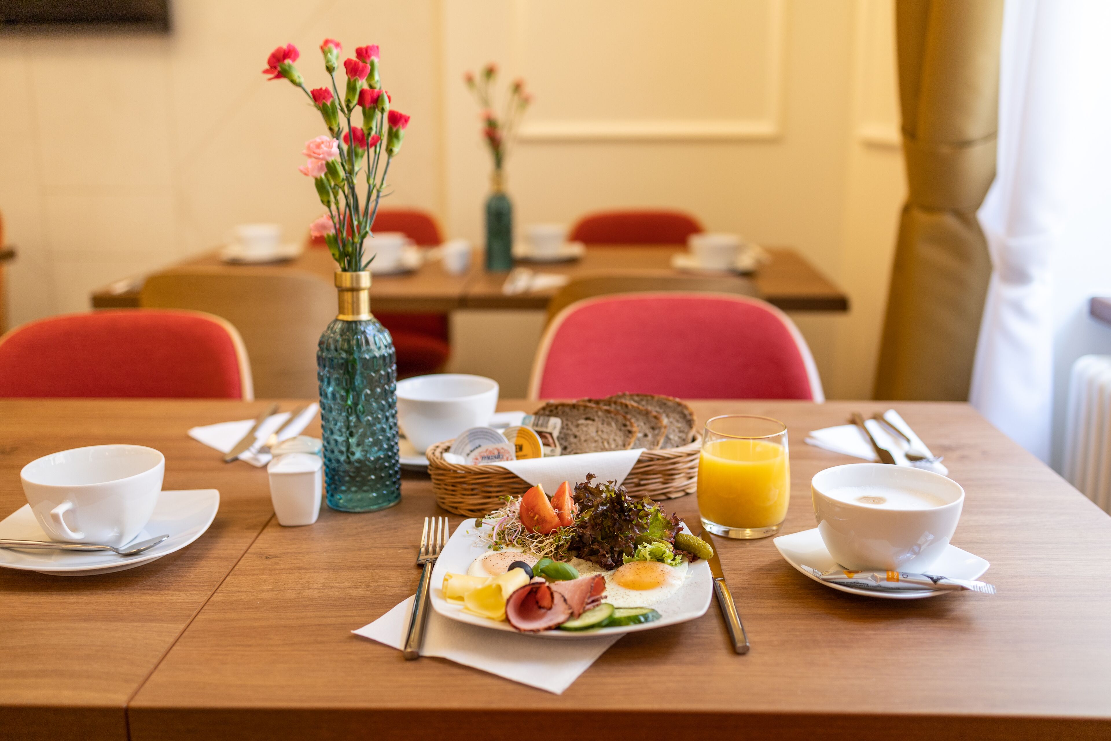 A breakfast setting with a wooden table, a vase of flowers, and a variety of breakfast items including eggs, vegetables, and toast.
