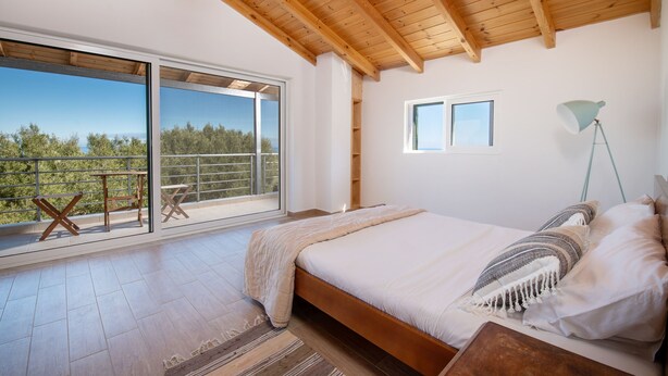 A bedroom with a large bed, a view through a sliding door to an outdoor balcony, and a wooden ceiling. - Villa Fioro (Zakynthos)