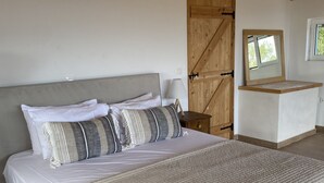 A bedroom with a large bed, a wooden door, an air conditioning unit, and a small window. - Villa Fioro (Zakynthos)