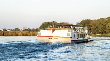 A riverboat with a flat deck and a covered upper deck, passengers seated, and a flag at the stern.