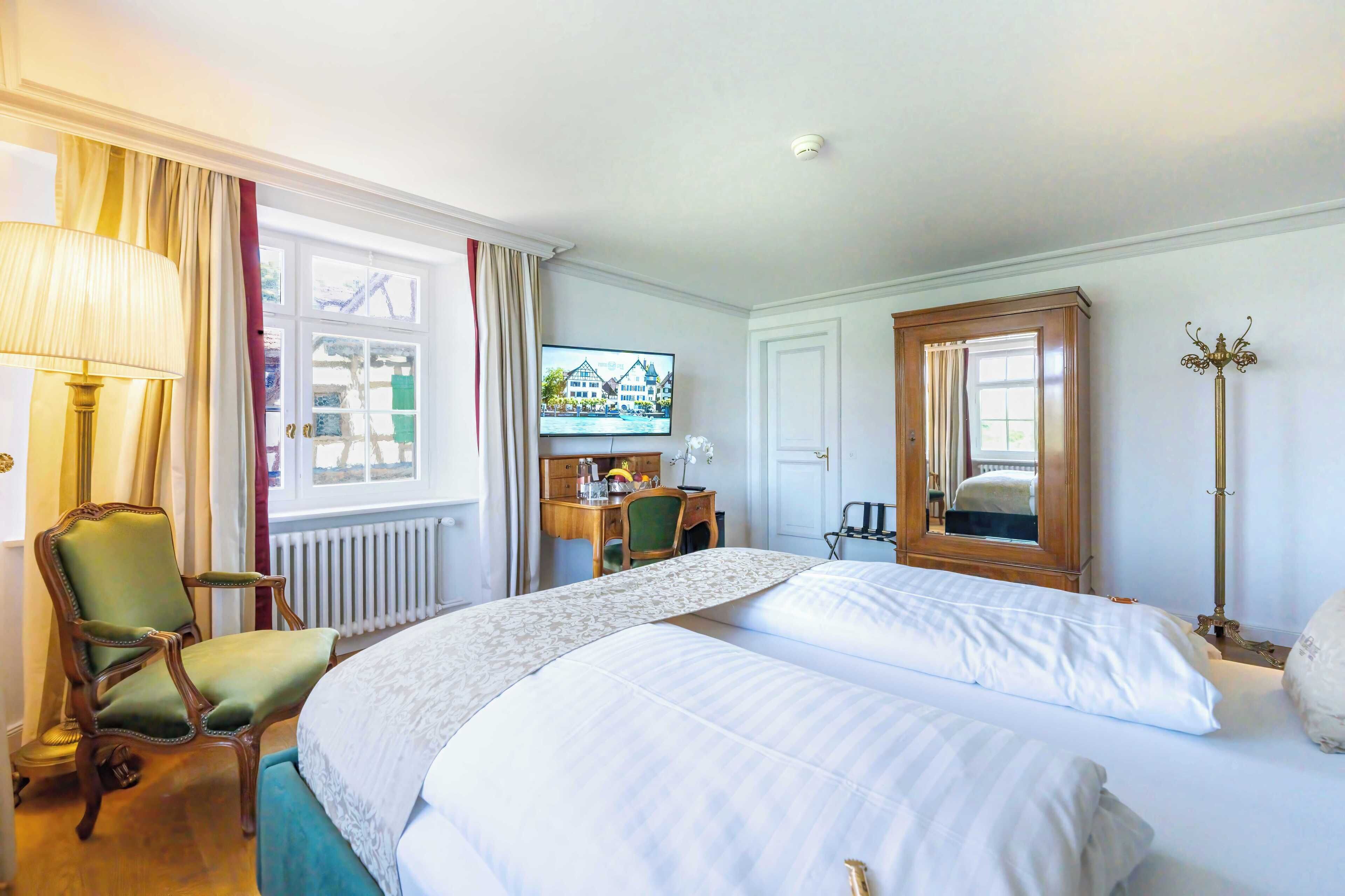 A hotel room with two beds, a desk, a chair, a television, and a mirror.