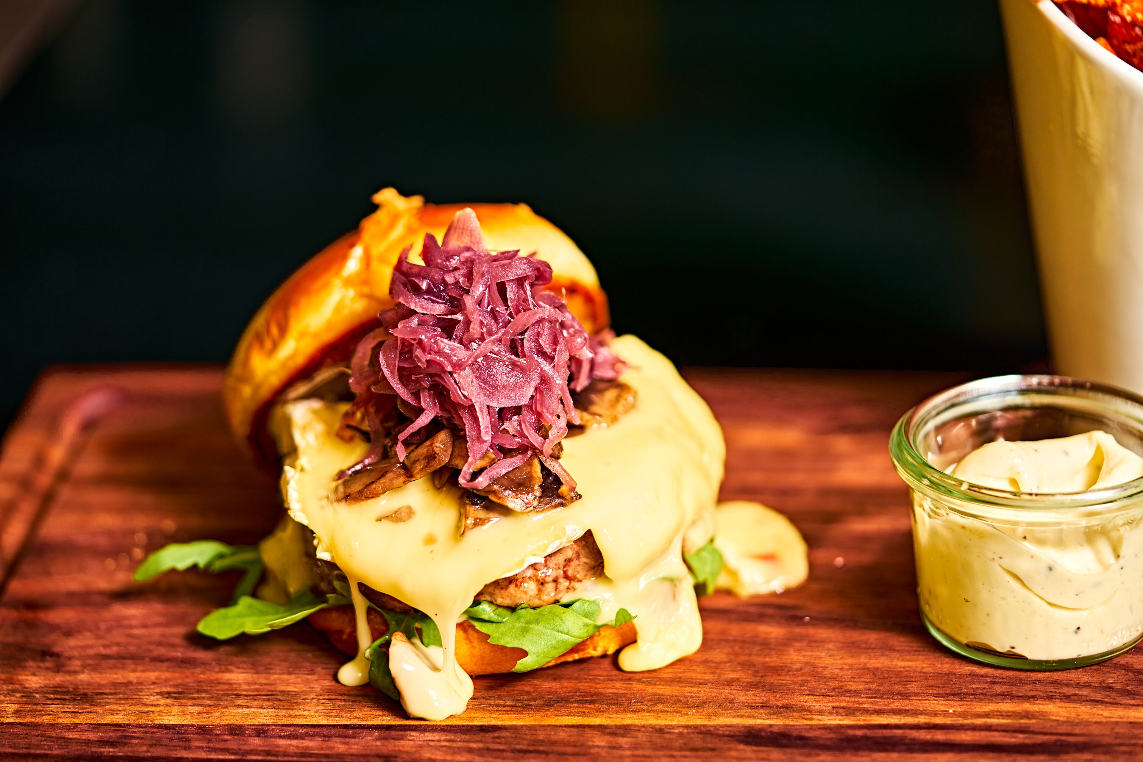 A sandwich with a side of sauce on a wooden surface.