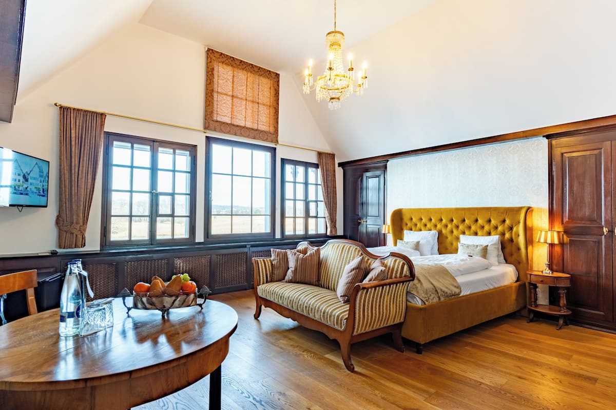A bedroom with a large bed, a sofa, a dining table with a pitcher, and a chandelier.