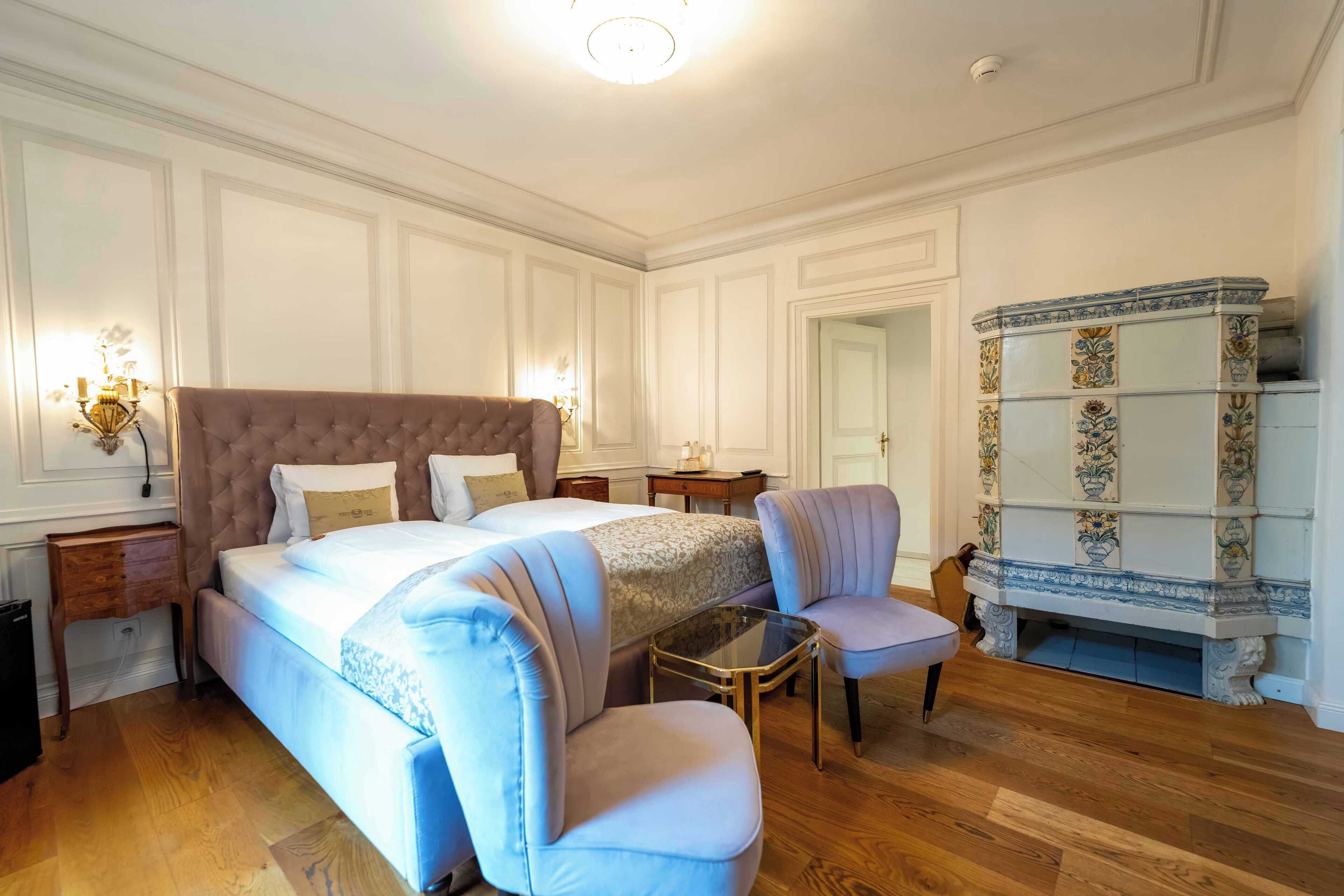 A bedroom with a large bed, two bedside tables, a chair, a small table, and a decorative cabinet.