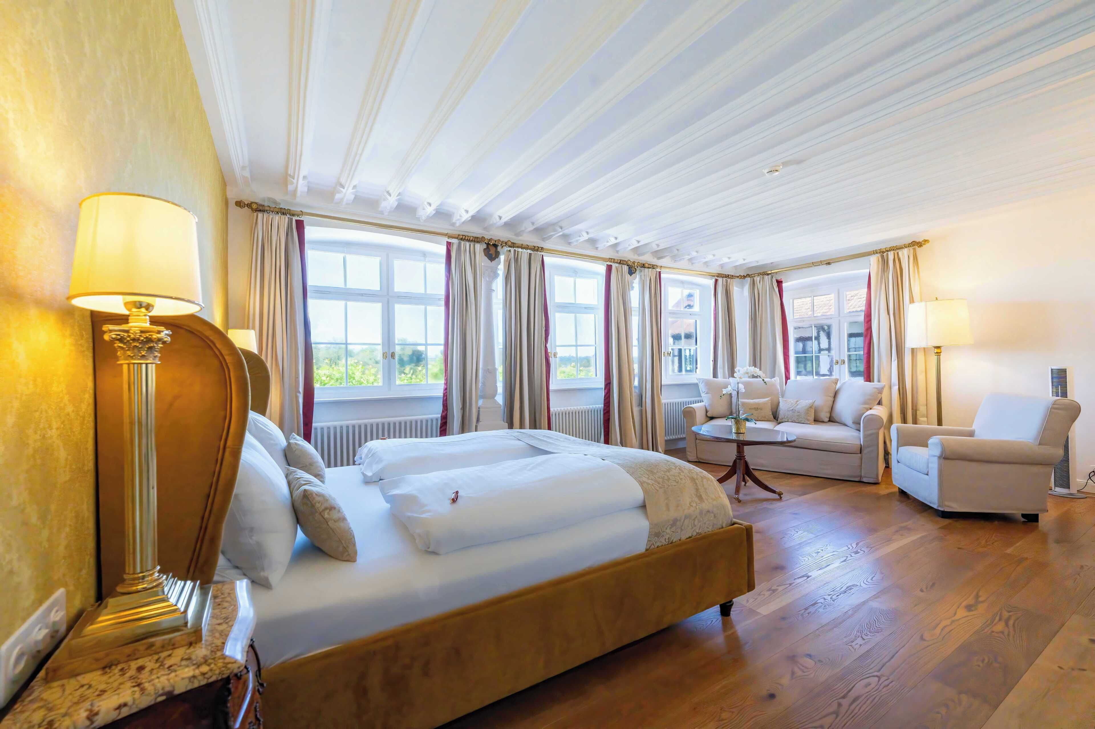 A hotel room with a large bed, two bedside tables with lamps, a sofa, and a chair.