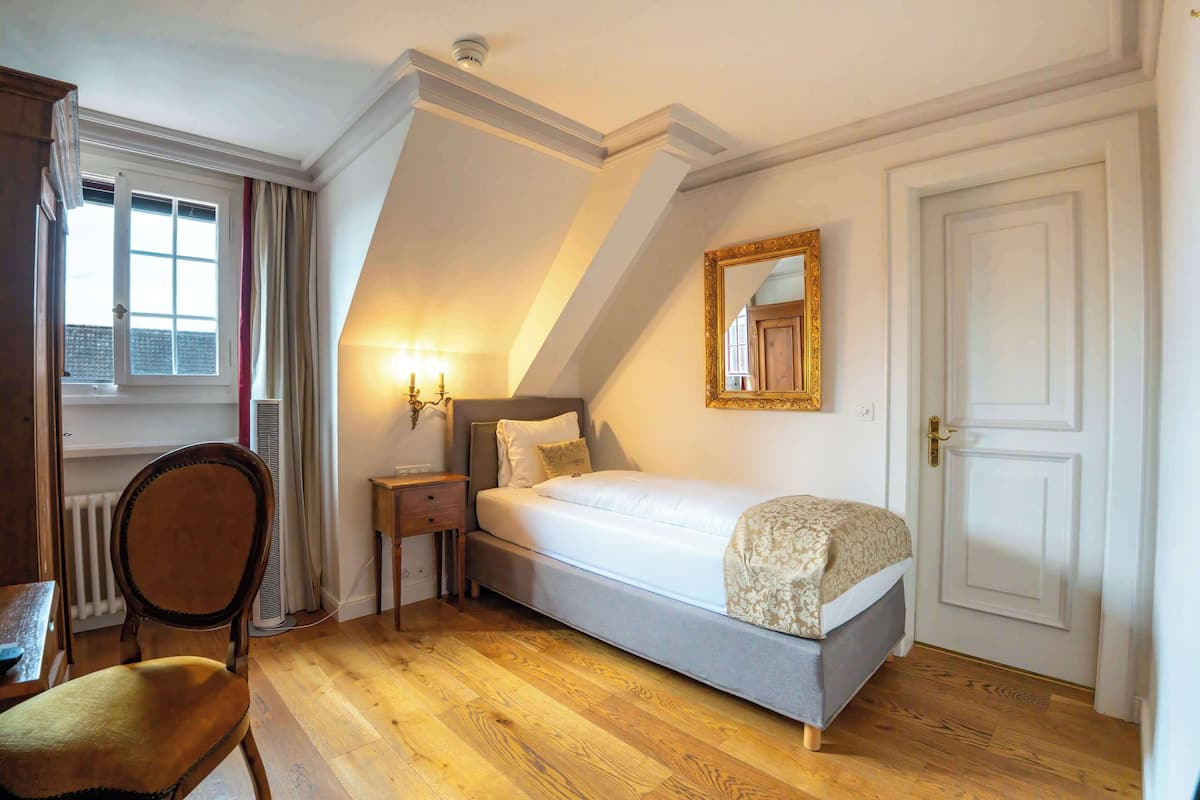 A bedroom with a bed, a chair, a nightstand, a mirror, and a door.