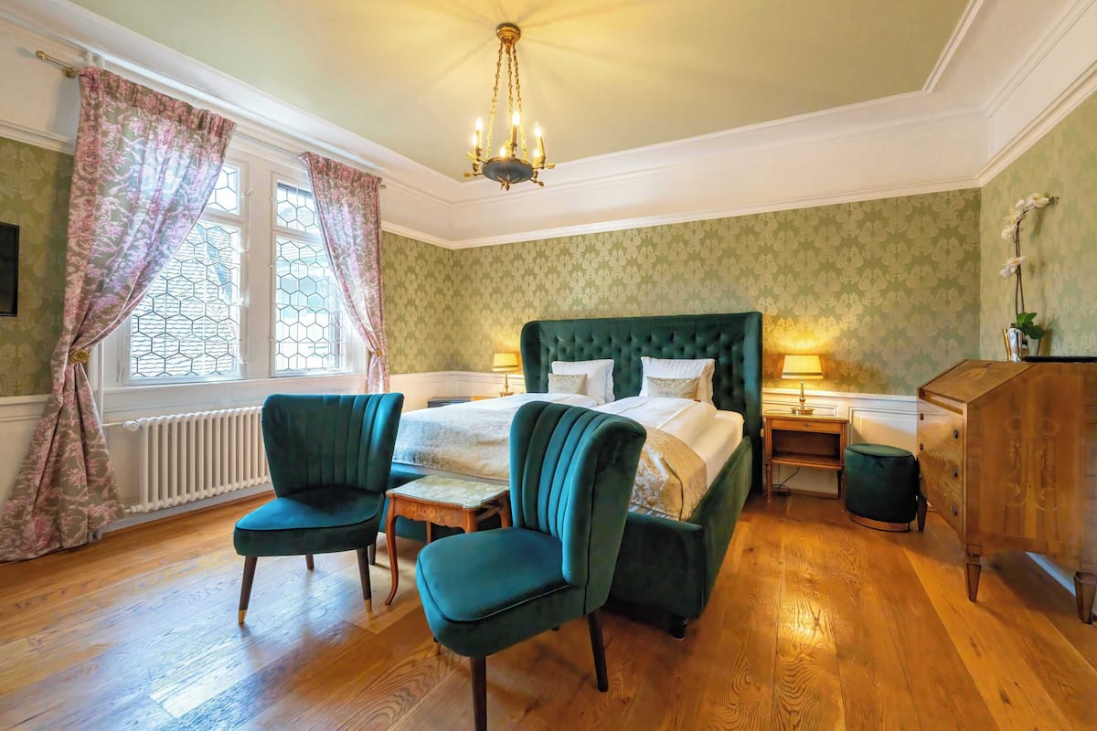 A bedroom with a large bed, two chairs, a wooden dresser, and a radiator.