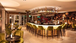 A bar area with a curved counter, green bar stools, and a variety of bottles and glasses. - Hotel Porto Sofie (Gottlieben)