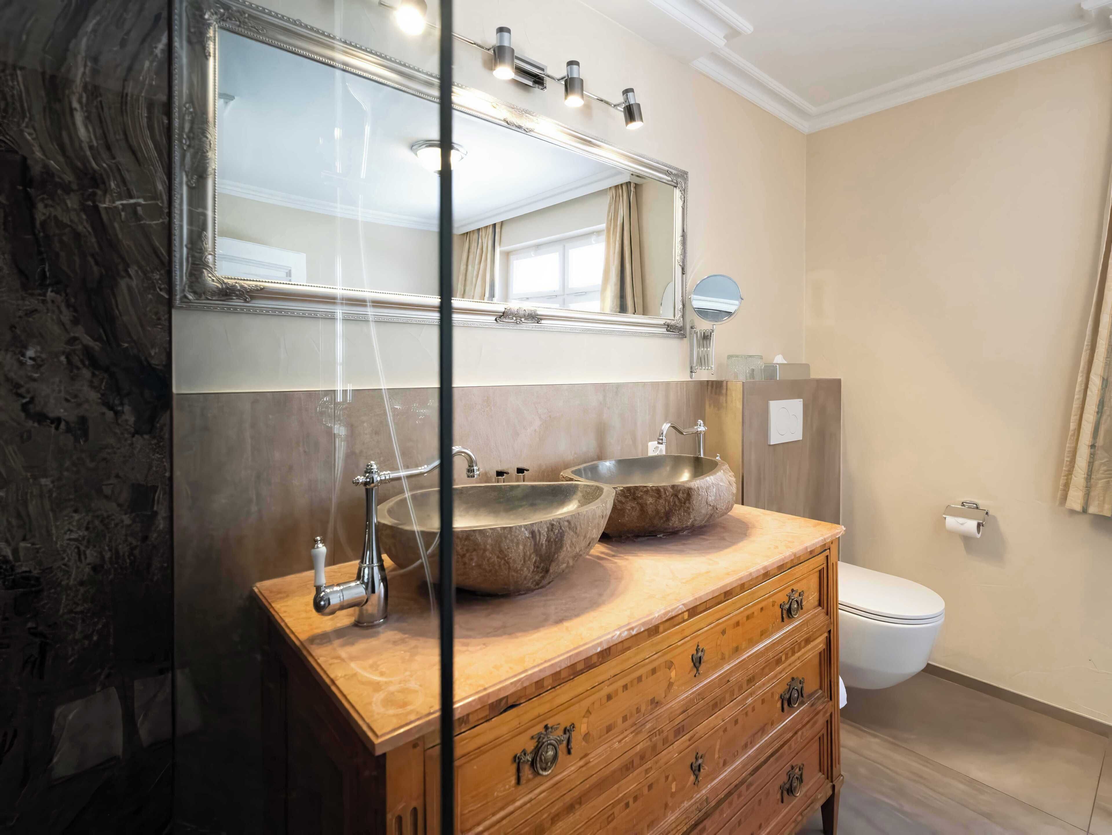 Ein Badezimmer mit einem Holzbadezimmerschrank, zwei Waschtüben, einem großen Spiegel und einer Toilette.