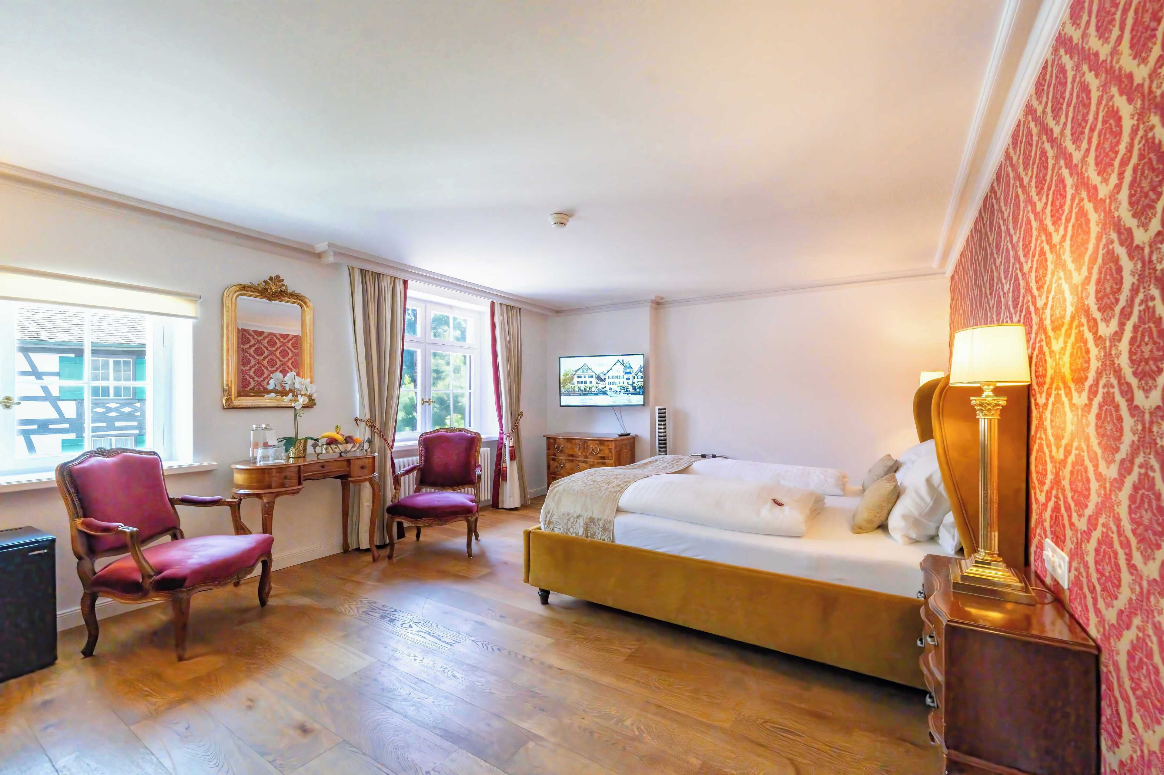 A hotel room with a bed, two chairs, a desk, a television, and a lamp.