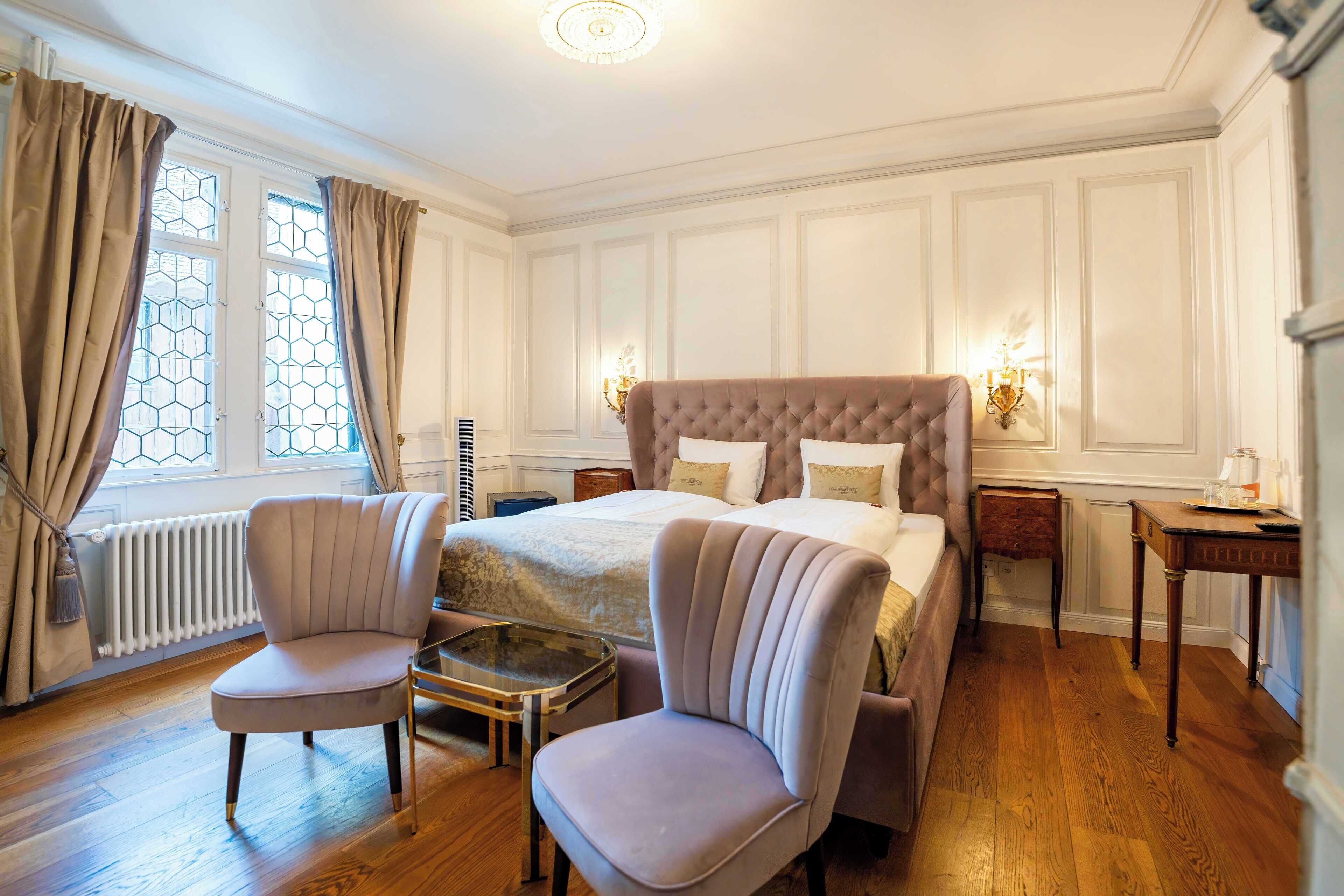 Quarto com cama grande, duas poltronas, uma mesinha e um criado-mudo.