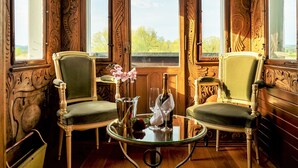 A room with ornate wood paneling, two green upholstered chairs, a glass table with a vase and wine glasses, and a chandelier. - Hotel Porto Sofie (Gottlieben)