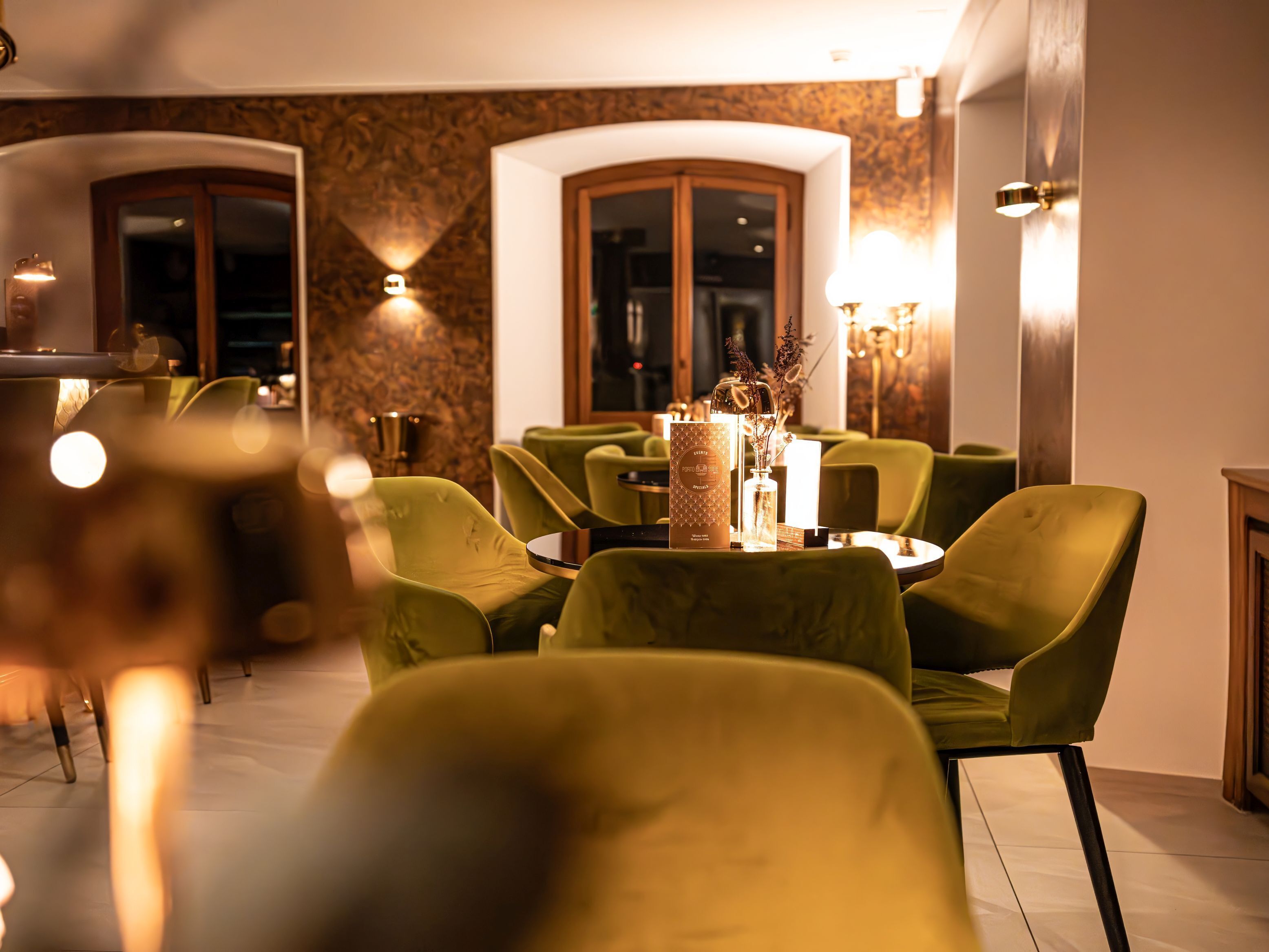 Un interior de restaurante con sillas tapizadas de verde, mesas redondas y un jarrón decorativo en el centro.