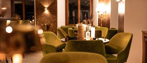 Un interior de restaurante con sillas tapizadas de verde, mesas redondas y un jarrón decorativo en el centro.