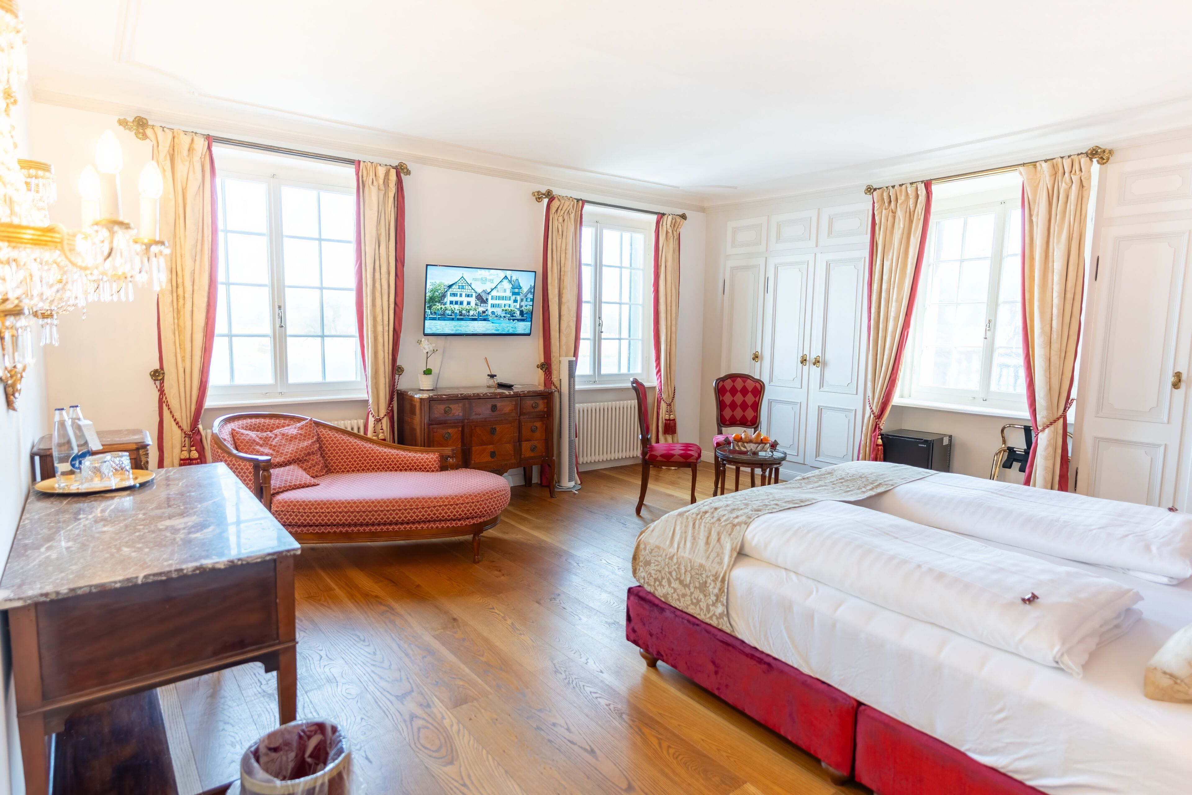 Une chambre bien éclairée, avec un grand lit, un bureau, une chaise et un téléviseur fixé au mur.