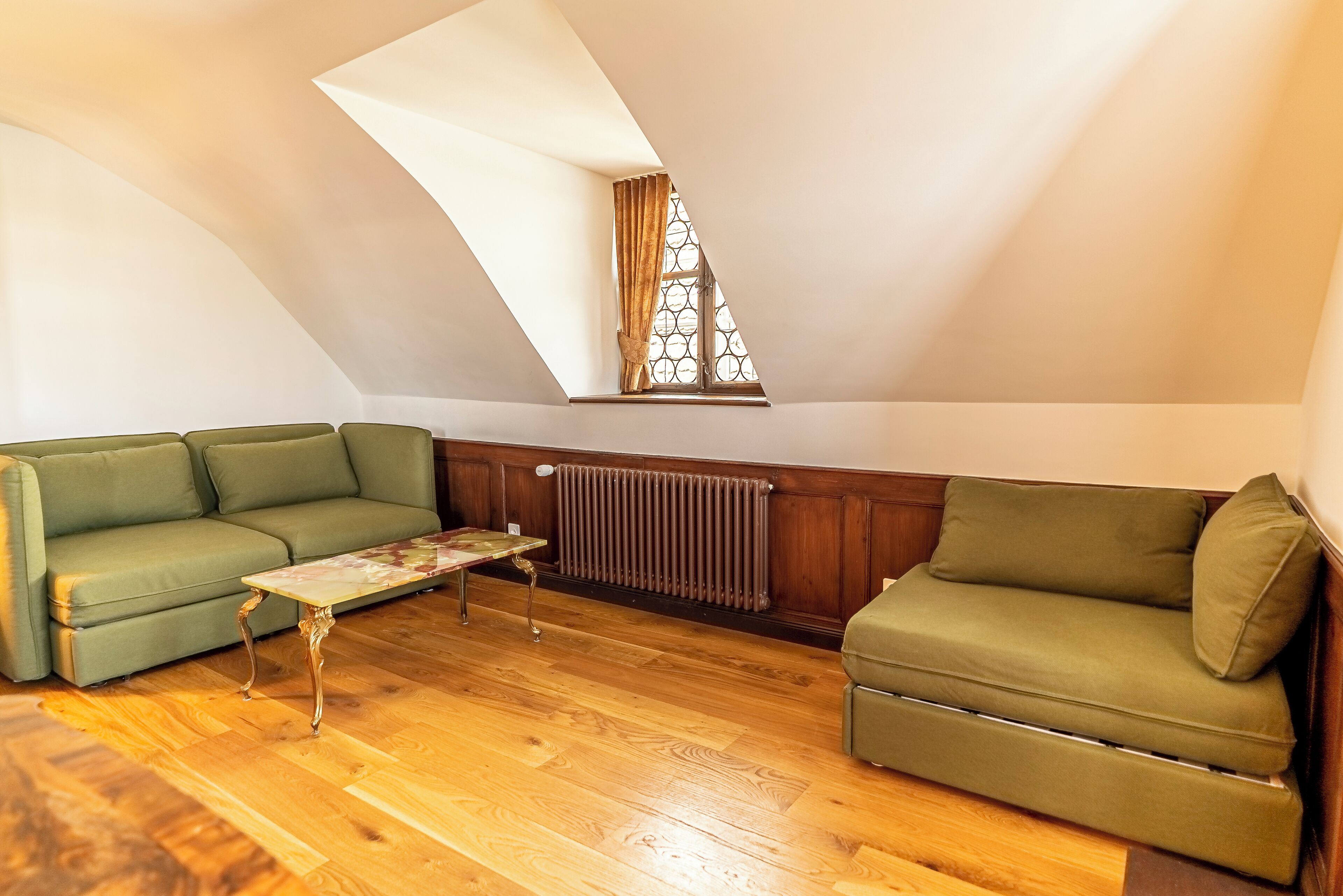 Une pièce de style loft avec un plafond en pente, un canapé vert, une petite table basse et un radiateur.