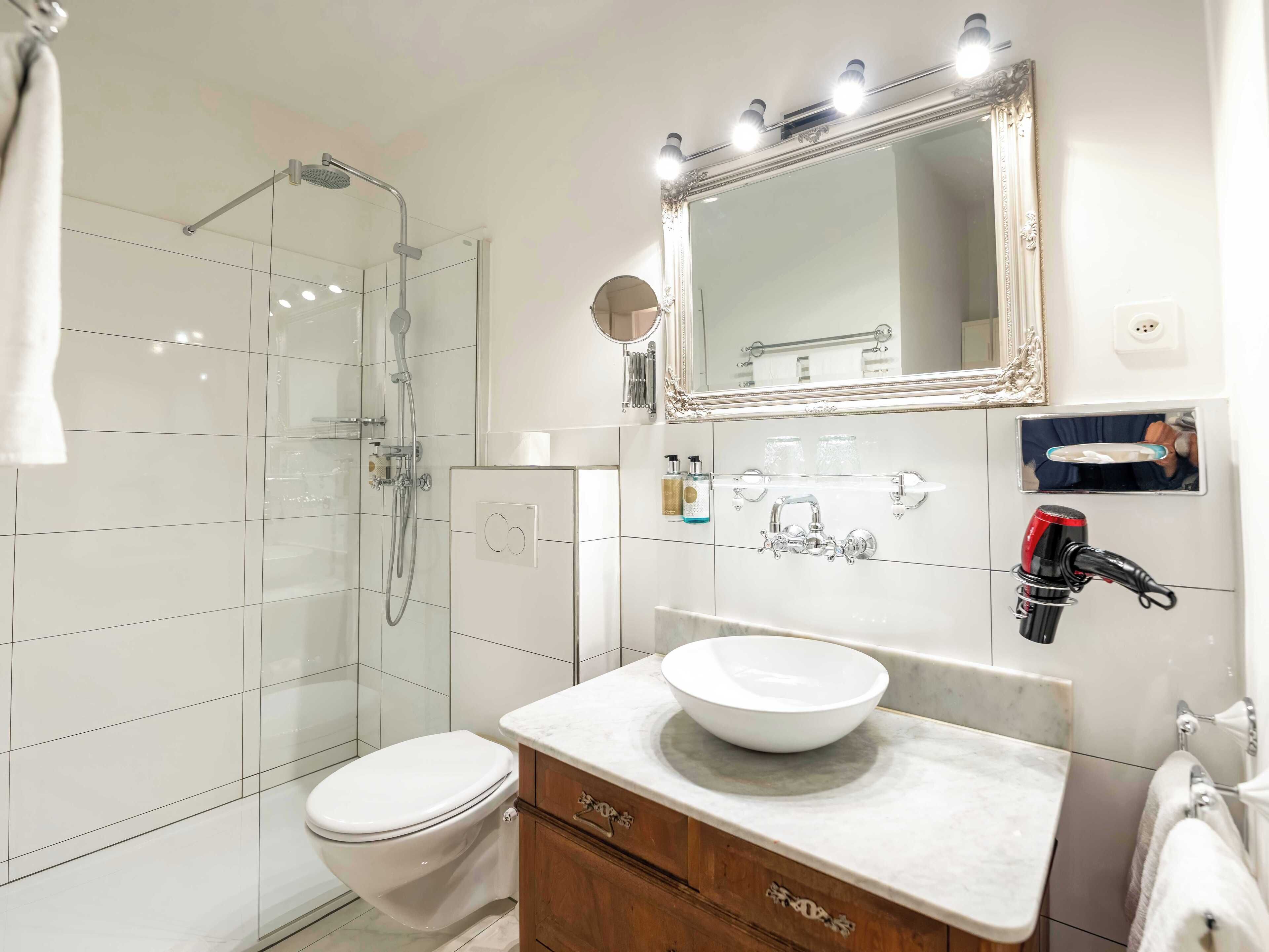 A modern bathroom with a glass shower enclosure, a white toilet, a vanity with a marble countertop, and a large mirror above the sink.