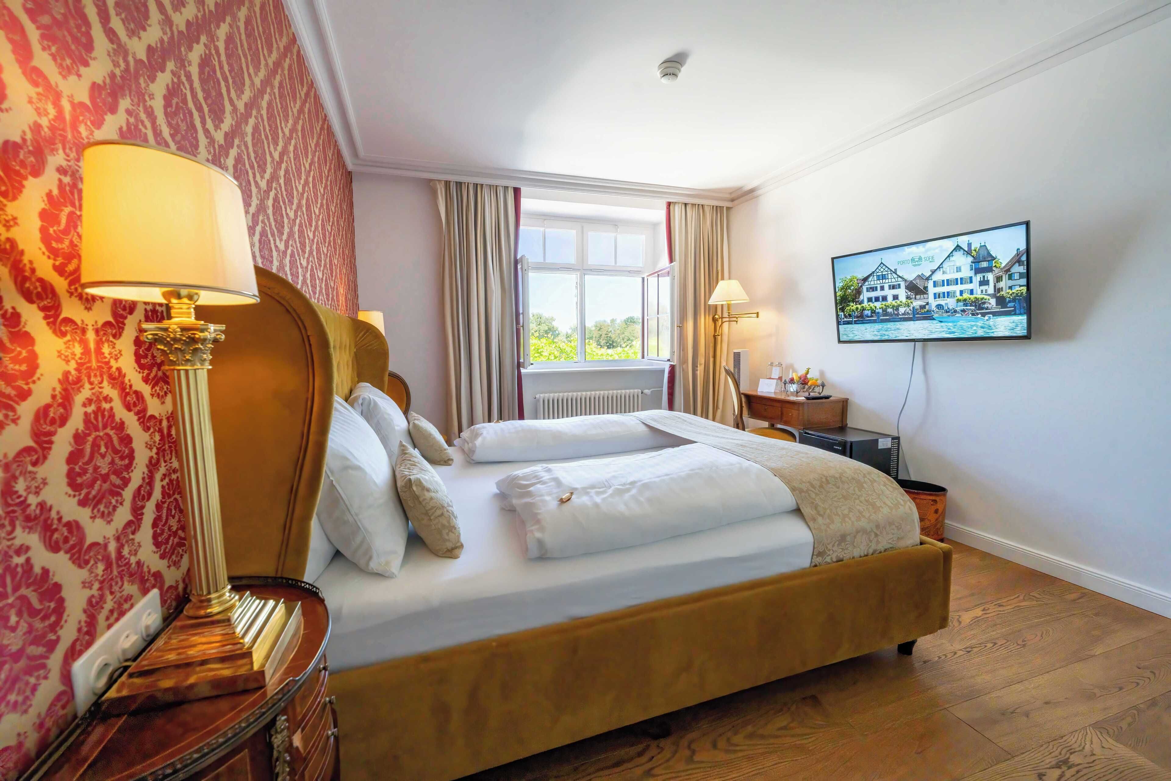 A hotel room with a large bed, two bedside tables, a TV mounted on the wall, and a window with curtains.