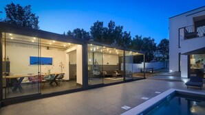 Une maison moderne dotée d’un patio entièrement vitré, d’une piscine et d’un coin repas aménagé avec du mobilier d’extérieur.