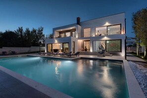 A modern two-story house with a swimming pool, lounge chairs, and a large window with a geometric design. - Villa Valdo (Loborika)