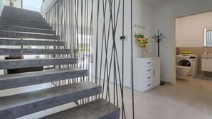 Un escalier moderne au design minimaliste, menant à une pièce où se trouvent un lave-linge et une petite plante.
