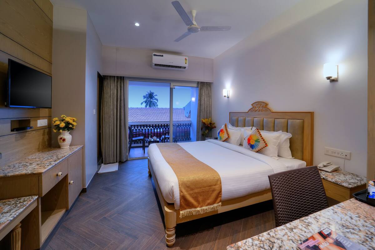 Habitación de hotel con cama, televisión, escritorio, silla, balcón con vistas y aire acondicionado.