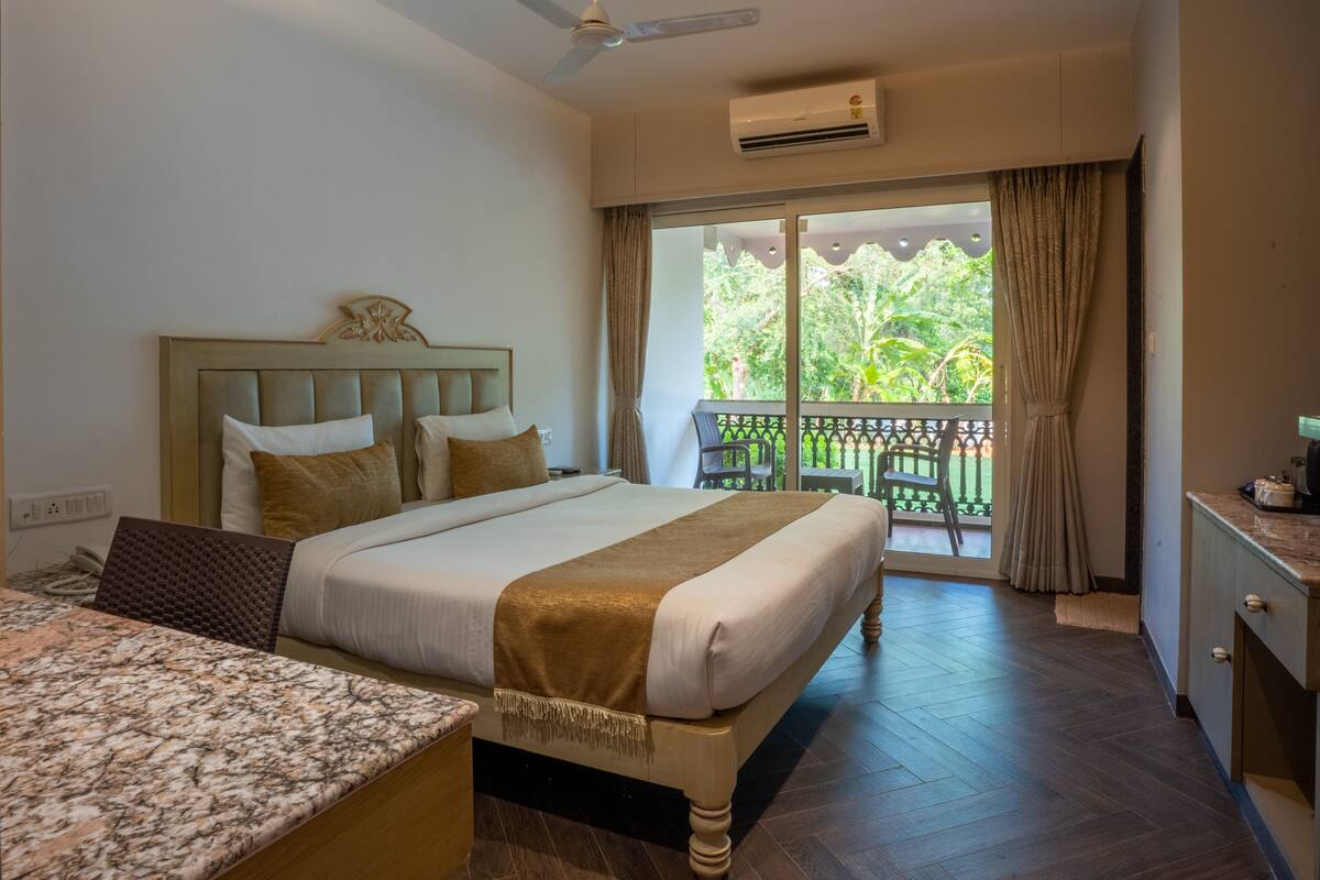 Habitación de hotel con cama, escritorio y balcón con vista a la vegetación.