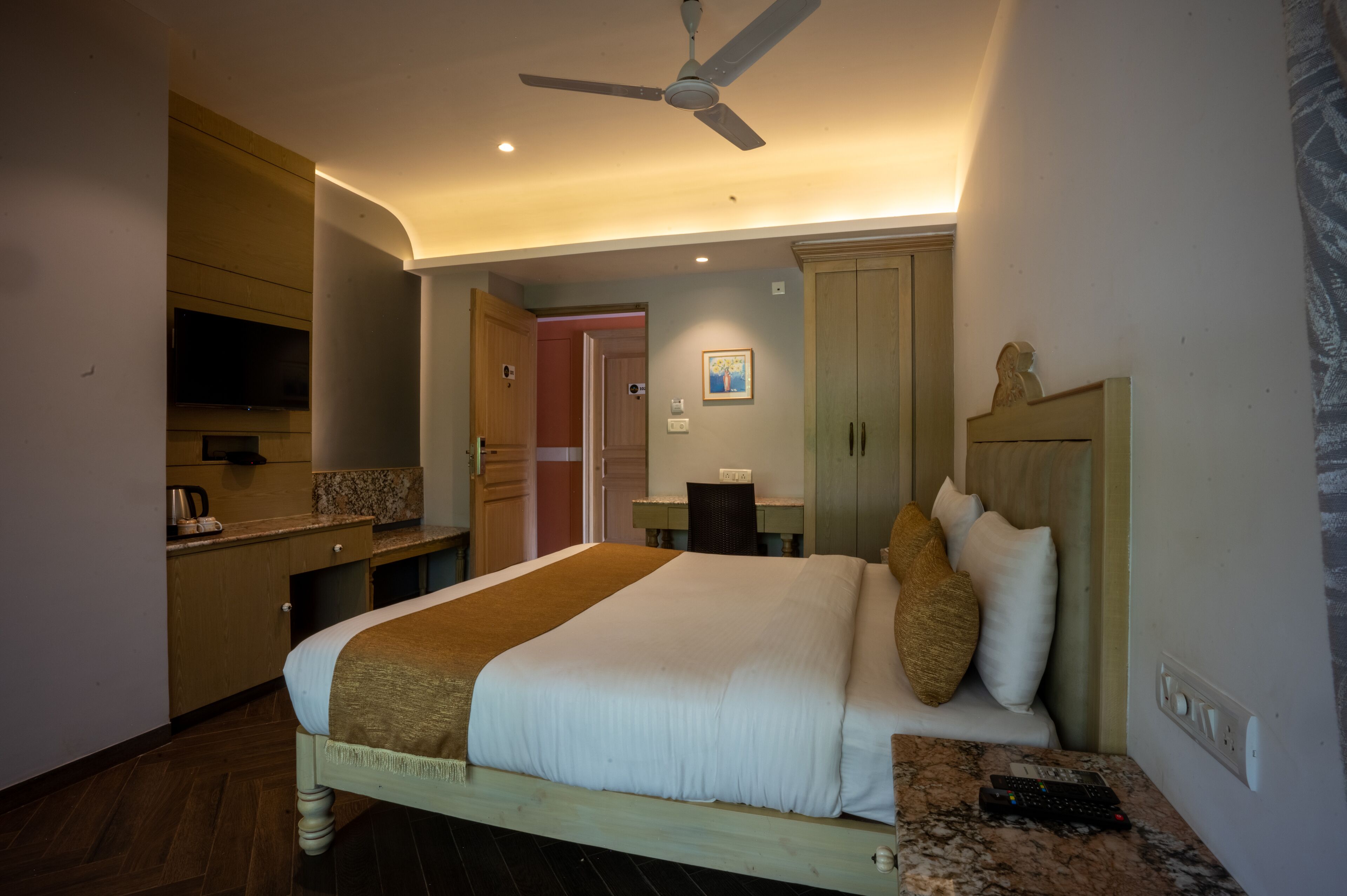 Habitación de hotel con cama, escritorio, silla, televisor y ventilador de techo.