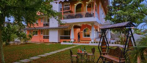 A two-story building with a balcony, a swing set, and a lawn.
