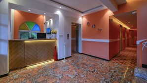 A hotel reception area with a herringbone-patterned counter, a reception desk, a digital screen, and a wall-mounted clock. - Foxoso Vega, Colva, Goa (Margao)