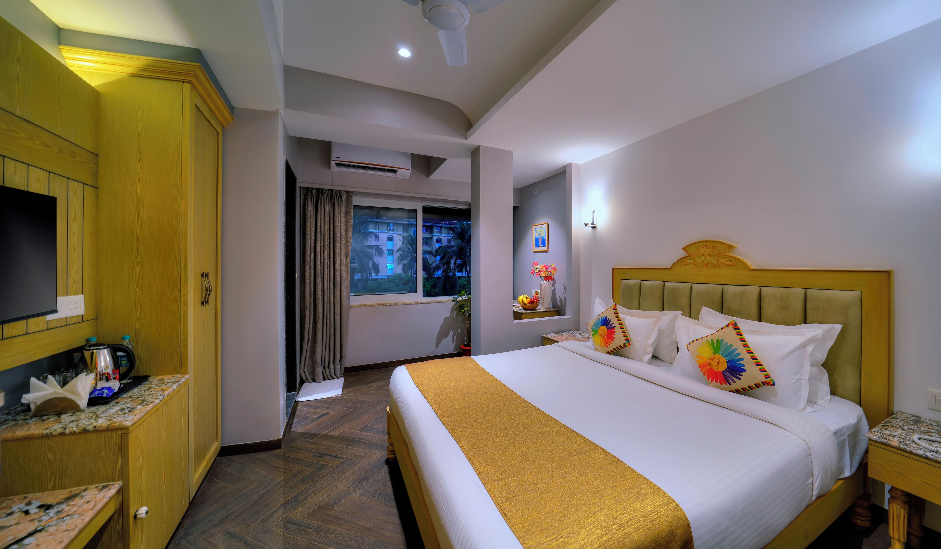 A hotel room with a bed, a TV, a desk, a window, and a ceiling fan.